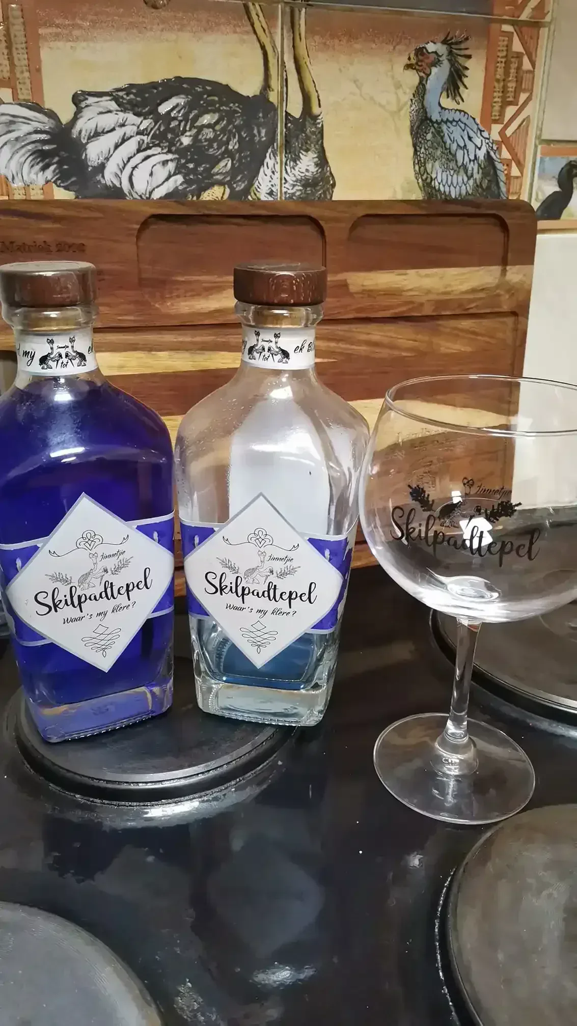 Twee Skilpadtepel bottels en 'n geëtiketteerde ballonglas op 'n stoof met ostrich-teël agtergrond